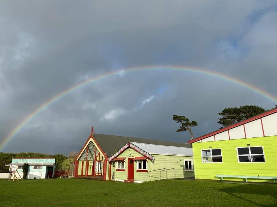 A rainbow arcing over the marae buildings at Pariroa Pā