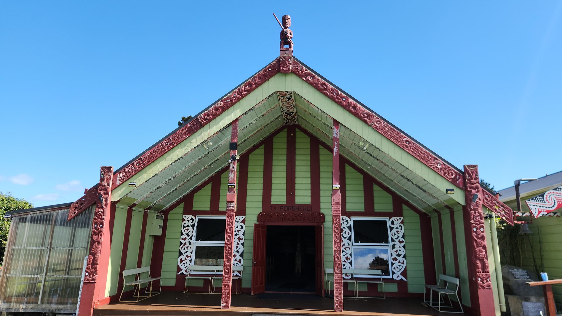 Exterior of the carved Taiporohēnui wharenui against a blue sky.
