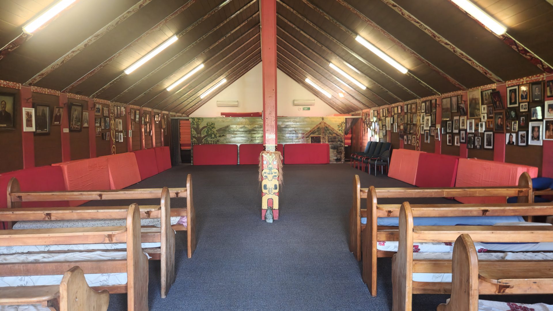 Wharenui interior with wooden seating and decorated walls.